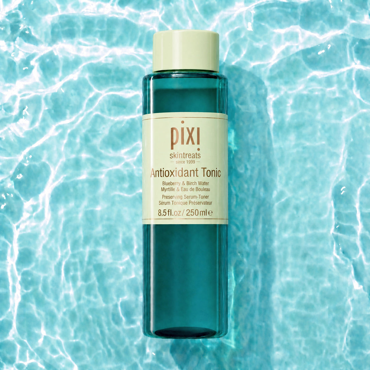 Pixi Skintreats Antioxidant Tonic in a translucent teal bottle with a cream-colored cap and label, centered against a background of rippling turquoise water.