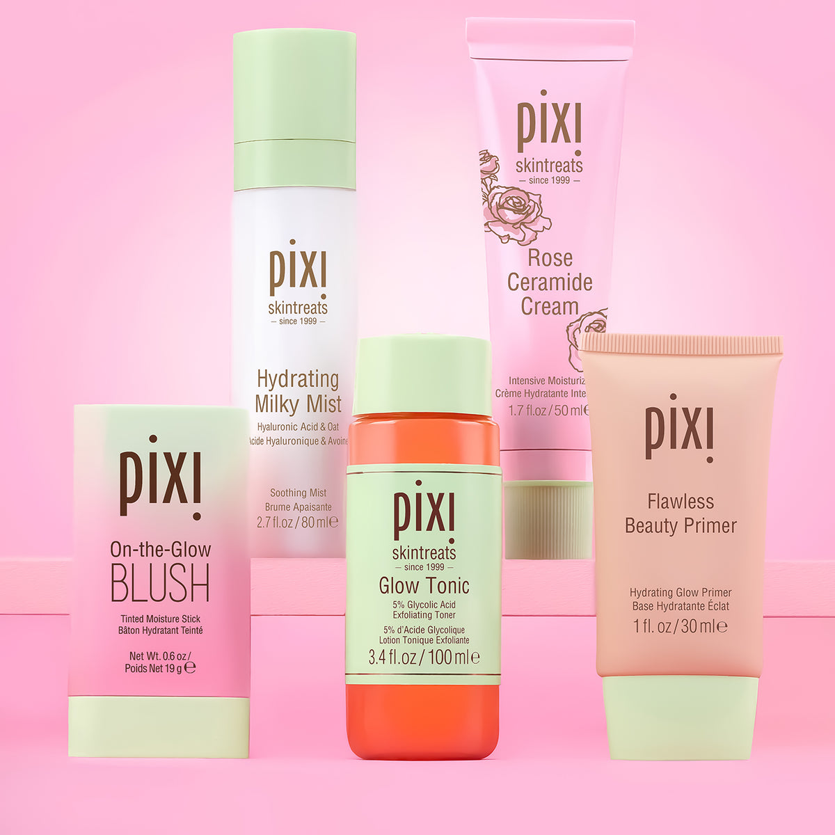 Six Pixi skincare and cosmetic products arranged together on a pink background. The products include Pixi Flawless Beauty Primer, Pixi On-the-Glow Blush, Pixi Glow Tonic, Pixi Hydrating Milky Mist, Pixi Rose Ceramide Cream.