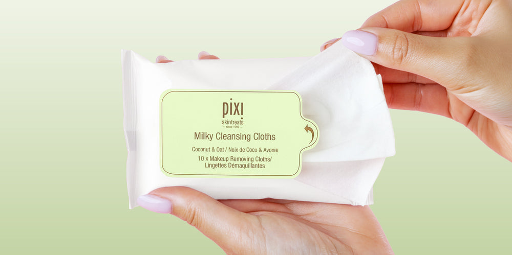Milky Cleansing Cloths on a green background being opened with a hand